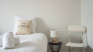 Un letto rifatto con cura, un cuscino con la scritta 'CANNES FLORELLA DEPUIS 1952', una lampada da comodino e una sedia bianca.