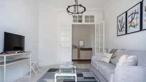 Un soggiorno moderno con televisore piatto, tavolino in vetro, divano grigio con cuscini decorativi e un lampadario.