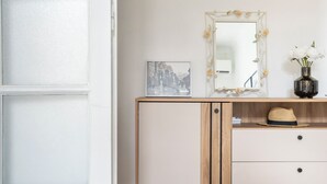 Una stanza con pavimento a scacchi, una porta bianca, una toeletta con specchio, un quadro e un vaso con fiori.