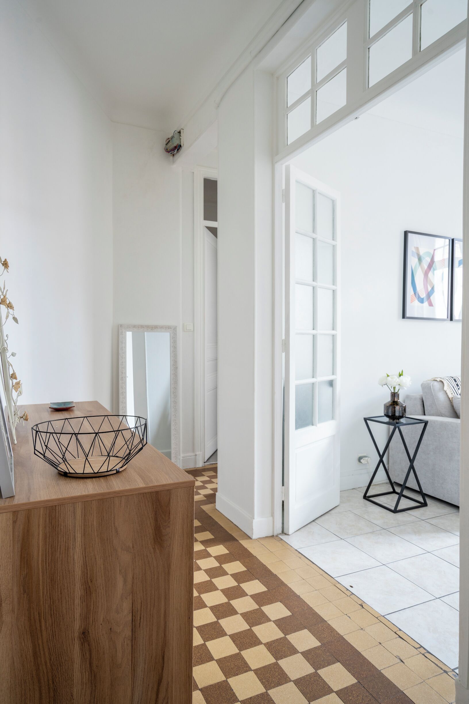 A modern interior with a wooden coffee table, a checkered floor, and a view into a living area with a sofa and a side table.