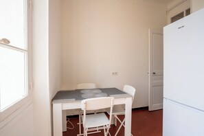 Eine kleine, weiße Küche mit Tisch, Stühlen, einem Kühlschrank und einem Fenster.