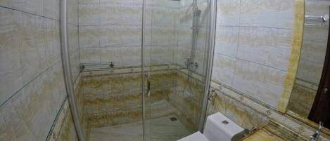 Een badkamer met een douchecabine van glas, een toilet en een houten wastafelmeubel met een spiegel.