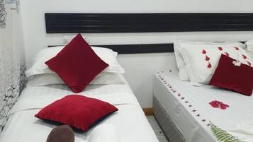A hotel room with two beds, each with white bedding and red pillows. There are two wall-mounted light fixtures and a visible wall decoration.