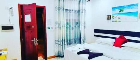 A hotel room with a bed, a desk, a chair, a door, and a window with curtains.