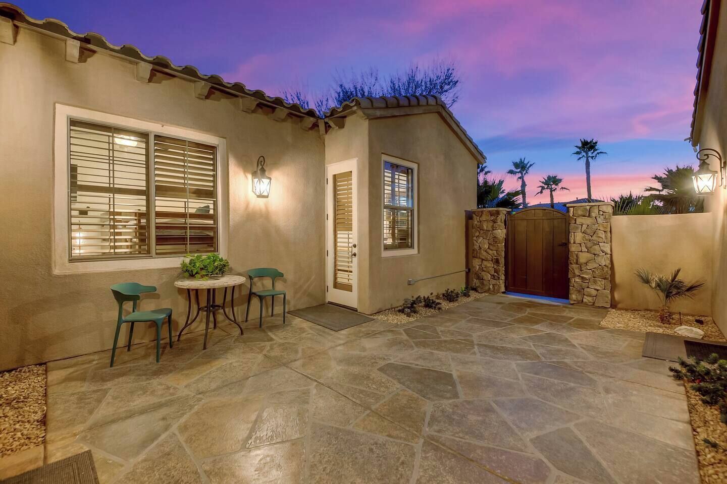 A patio with stone flooring, a table with chairs, and a gated entrance.