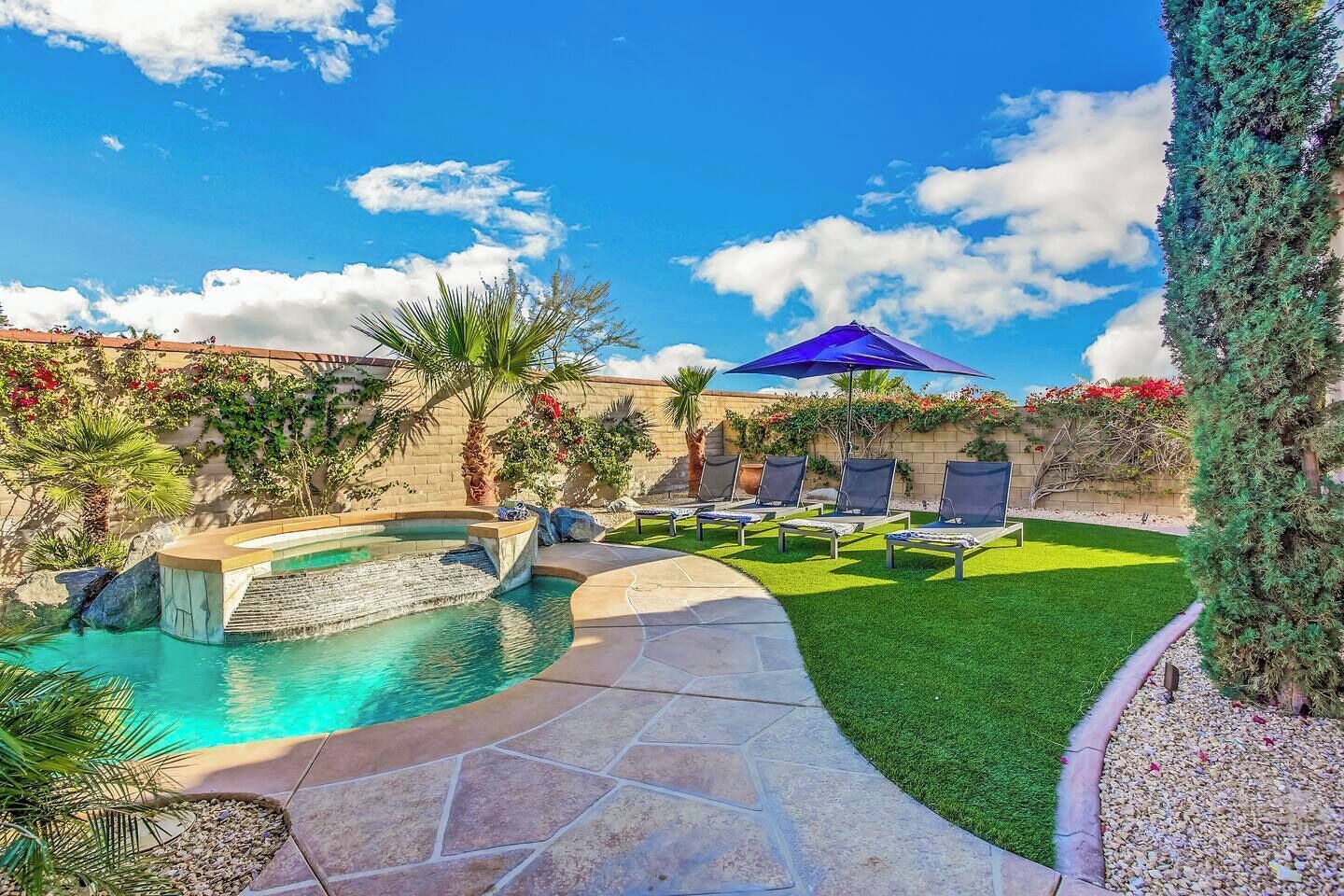 A backyard with a swimming pool, a small waterfall, and a seating area with umbrellas.