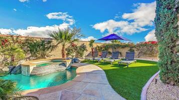 A backyard with a swimming pool, a small waterfall, and a seating area with umbrellas.