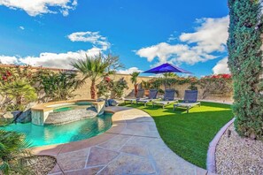 Ein Garten mit Swimmingpool, kleinem Wasserfall und einer Sitzecke mit Sonnenschirmen.