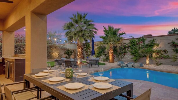 An outdoor dining area with a pool, palm trees, and a sunset.