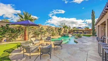A pool area with lounge chairs and umbrellas, surrounded by landscaped gardens and a clear sky.