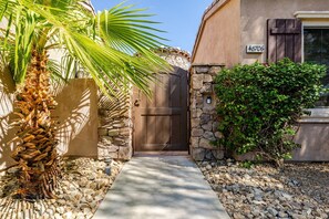A stone wall, a palm tree, and a house with a number sign.