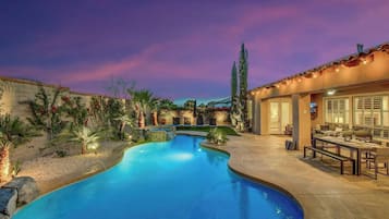A swimming pool with a curved design, surrounded by a patio area with outdoor furniture and a building with a tiled roof.