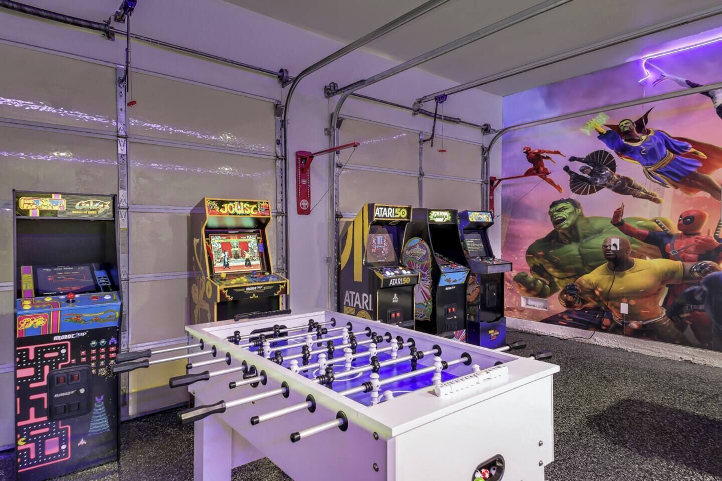 A room with a foosball table, arcade games, and a mural of comic book characters.