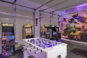 Ein Raum mit einem Kicker, Spielautomaten und einem Wandbild mit Comicfiguren.