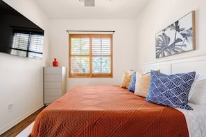 A bedroom with a bed, a window, a dresser, and a wall-mounted artwork.