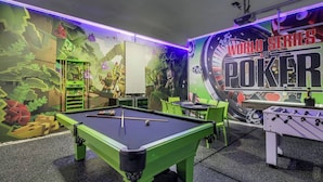 A pool table with a green frame, a foosball table, and a mural with the text 'WORLD SERIES POKER'.