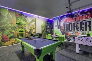 A pool table with a green frame, a foosball table, and a mural with the text 'WORLD SERIES POKER'.