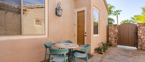 Una casa con patio, una mesa con sillas, una puerta de madera y un muro de piedra.