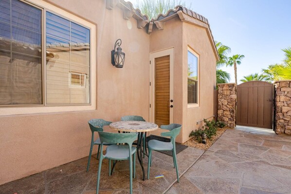 A house with a patio, a table with chairs, a wooden door, and a stone wall.