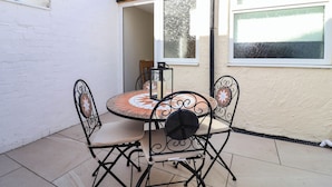 Eine Terrasse mit einem runden Tisch, vier Stühlen, einem Fenster und einer weißen Wand.