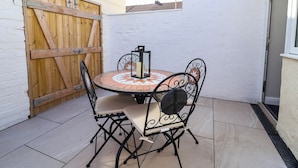 Eine Terrasse mit rundem Tisch und vier Stühlen, einem hölzernen Tor und einer weißen Mauer.