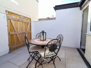 A patio with a round table and four chairs, a wooden gate, and a white wall. - Brightside (Wirral)