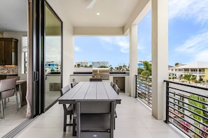 Ein Balkon mit Esstisch und Stühlen, einem Grill und Blick auf Gebäude und Palmen.