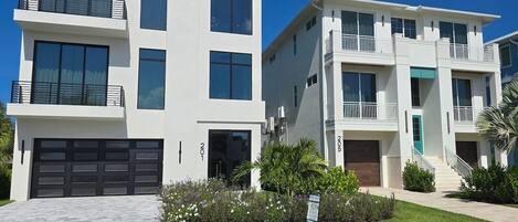 A modern two-story residential building with a garage, balconies, and a well-maintained lawn.