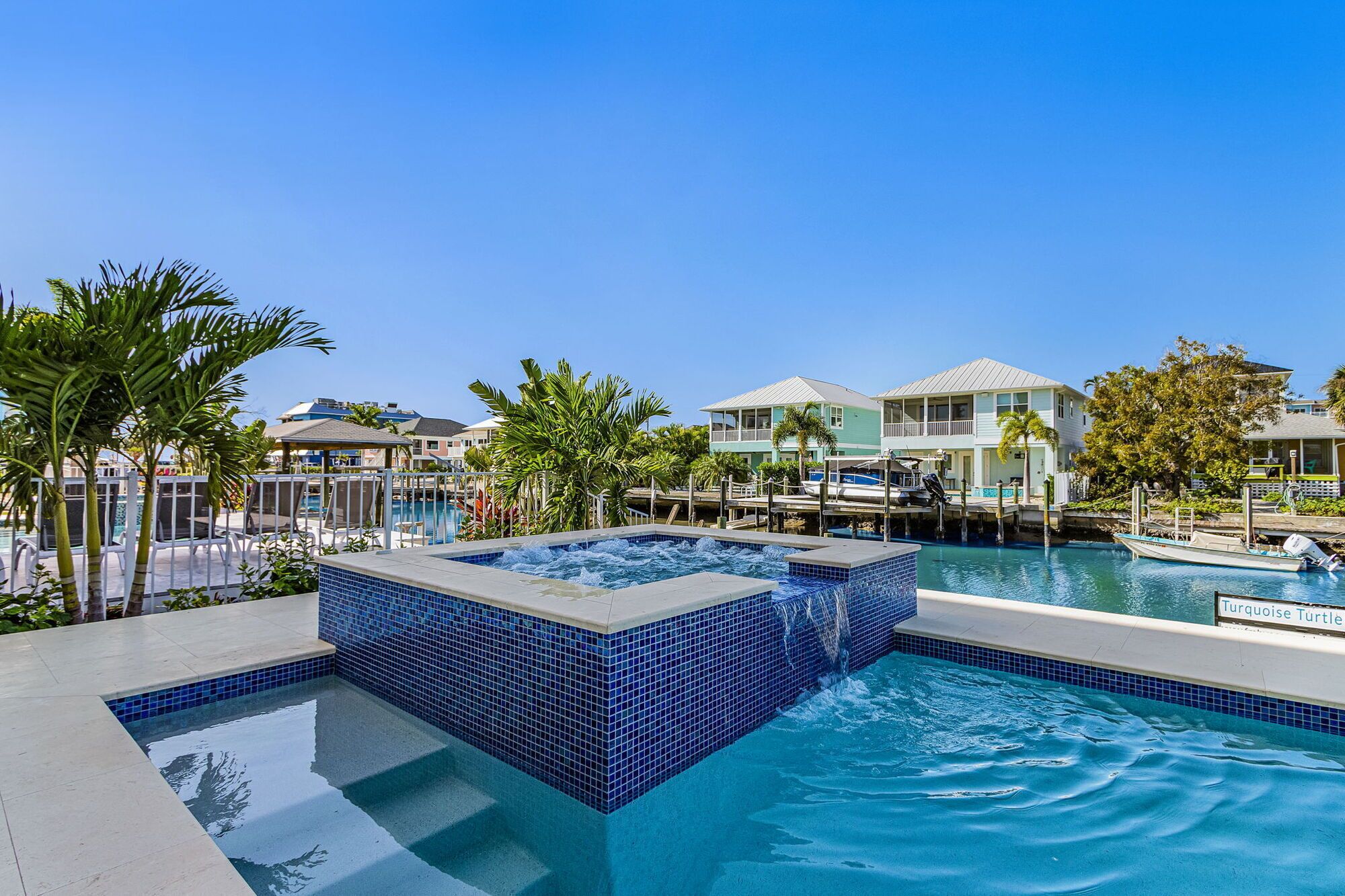 A swimming pool with a hot tub, surrounded by palm trees and a clear blue sky.