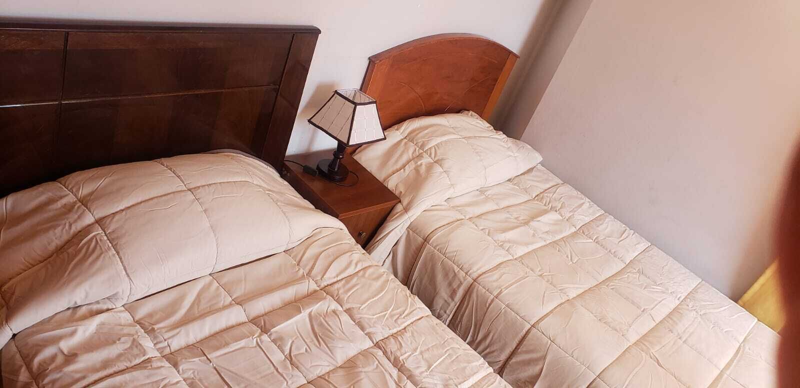 Een tweepersoonsbed met een houten hoofdbord en nachtkastje met een lamp.