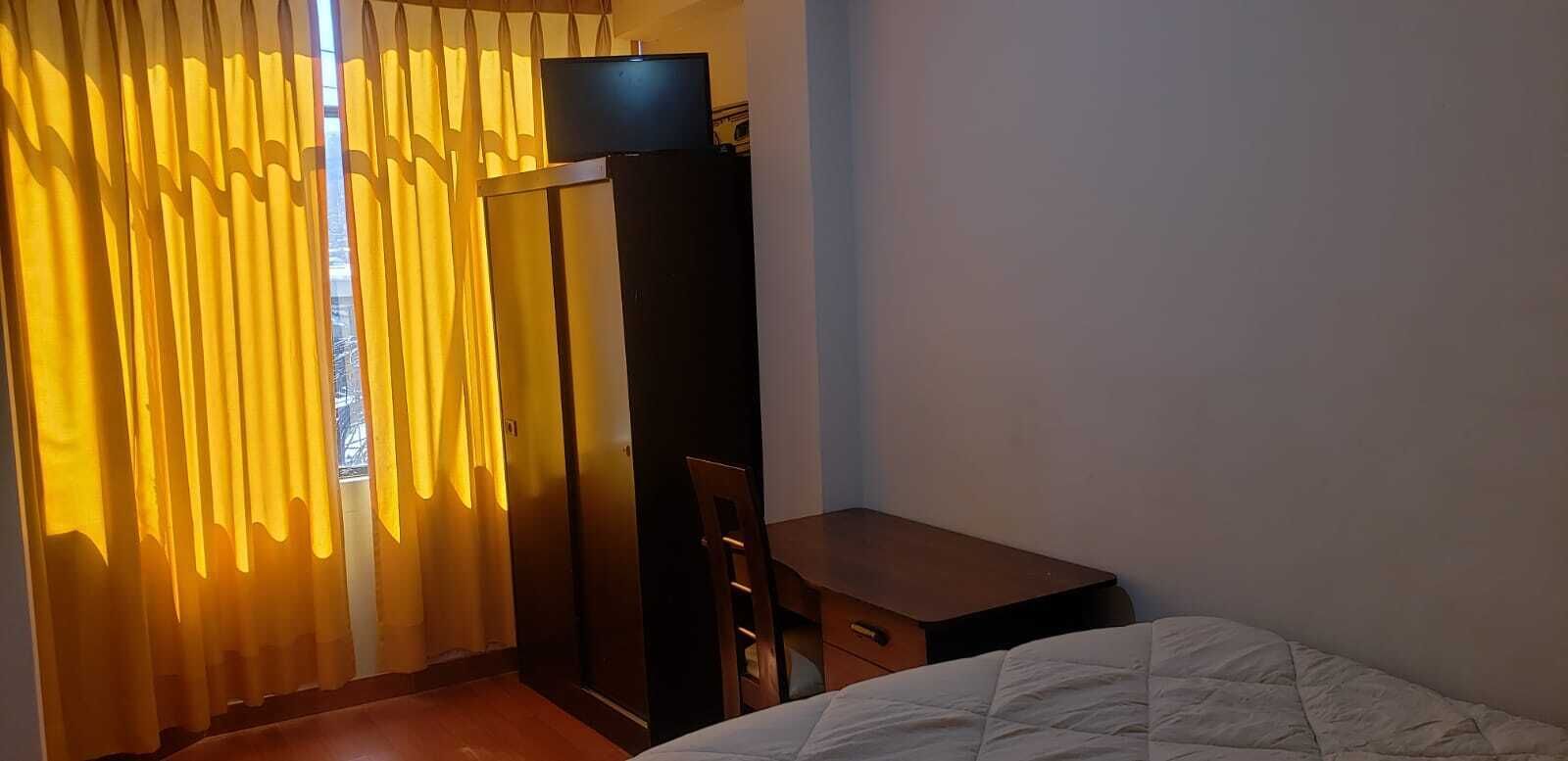 Ett hotellrum med en säng, ett skrivbord, en tv-apparat på ett skåp och ett fönster med gardiner.