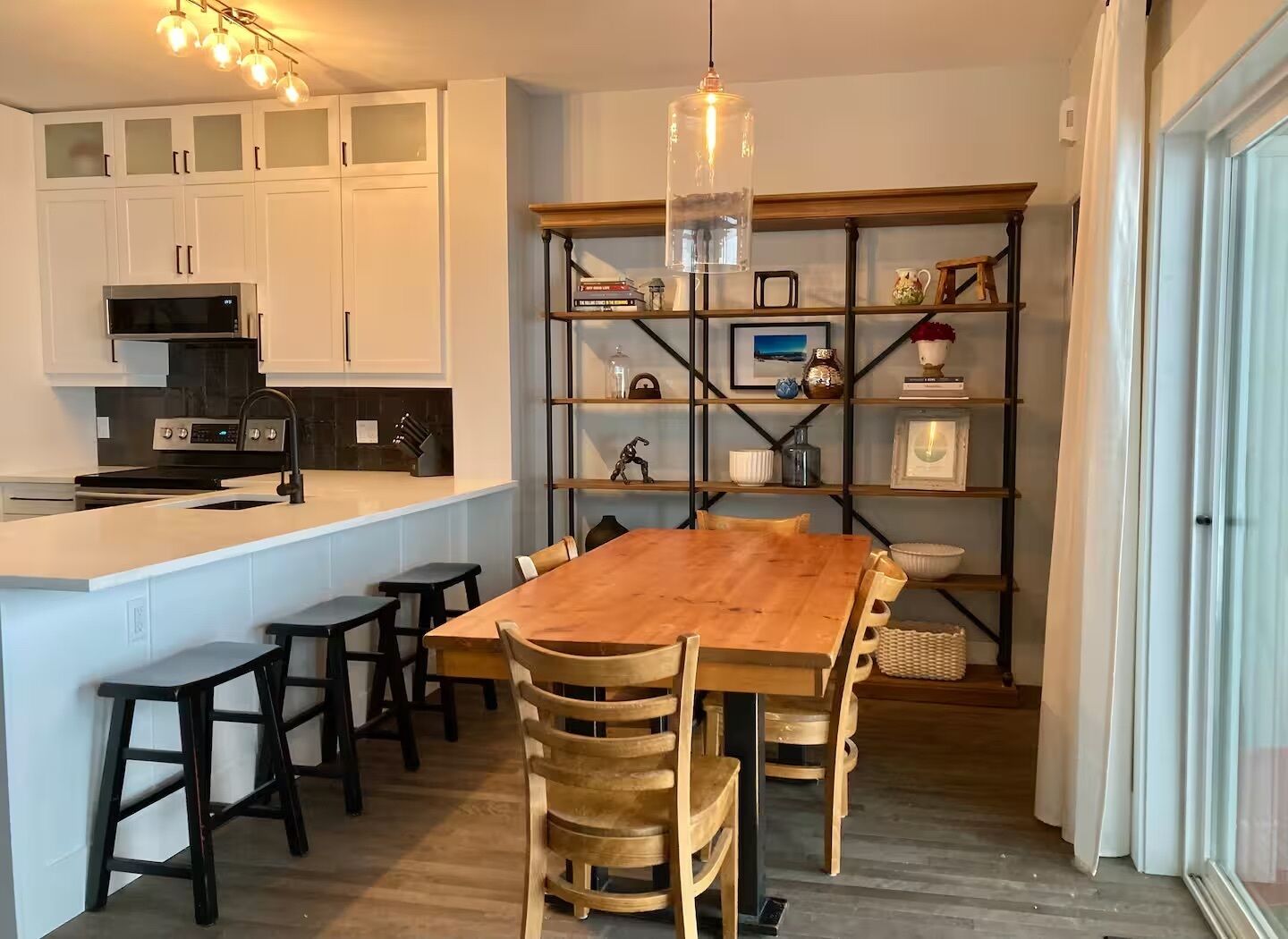 A modern kitchen with white cabinets, a wooden dining table, and a built-in bookshelf.