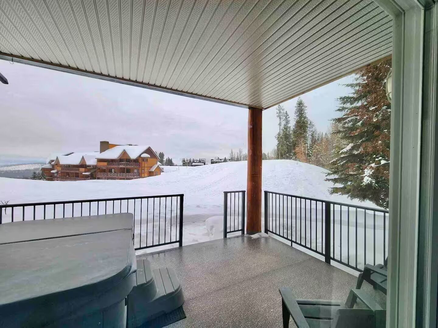 A covered outdoor area with a table and chairs, a view of a snow-covered landscape, and a building in the distance.