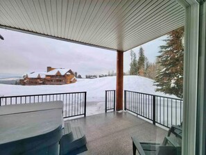 Un espacio al aire libre techado con una mesa y sillas, vista a un paisaje cubierto de nieve y un edificio en la distancia.