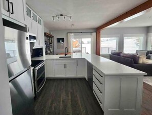 A modern kitchen with white cabinetry, a stainless steel refrigerator, and a large island with a sink. - Ski-In/Ski-Out / Private Hot Tub & Mountain Views (Kimberley)
