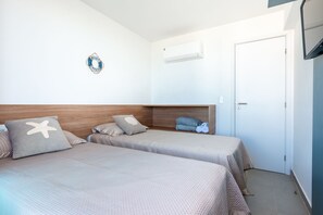 Une chambre d’hôtel avec deux lits, une tête de lit en bois, un climatiseur fixé au mur, une porte et une petite étagère avec des serviettes.