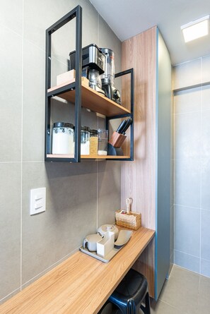 Une cuisine moderne dotée d’une machine à café intégrée, d’une étagère en bois où sont rangés les ustensiles de cuisine, et d’un plan de travail agrémenté d’un panier et de différents récipients.