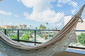A hammock tied to a balcony railing overlooking a residential area with palm trees and buildings. - Apê Completo em Porto de Galinhas-SH164D (Ipojuca)