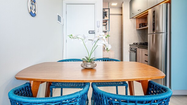 Une cuisine moderne avec un réfrigérateur en acier inoxydable, une table à manger avec des chaises bleues et des orchidées blanches disposées sur la table.