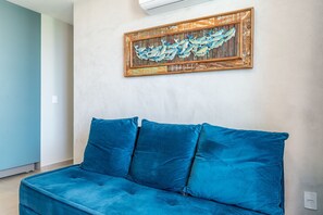 Une pièce avec un canapé bleu, une œuvre d’art accrochée au mur et un interrupteur.