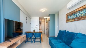 Un espace de vie moderne comprenant un canapé bleu, une table à manger en bois avec des chaises bleues, un téléviseur et un coin cuisine.