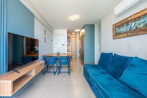 Ein modernes Wohnzimmer mit einem blauen Sofa, einem Holzesstisch mit blauen Stühlen, einem Fernseher und einer Küchenzeile.