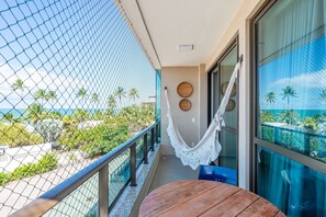 Un balcon avec vue sur l’océan, un hamac et une table en bois.