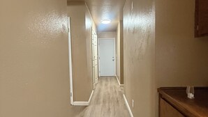 A narrow hallway with wooden flooring, beige walls, and a white door at the end.