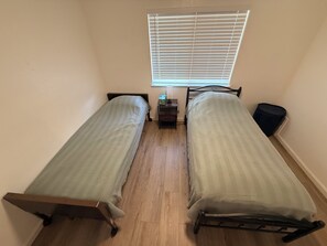 A room with two single beds, a small table, and a window with blinds.