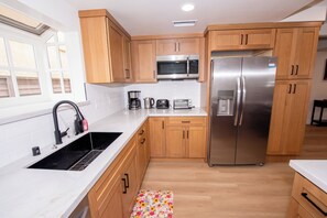 A modern kitchen with wooden cabinets, stainless steel appliances, a microwave, a refrigerator, a coffee maker, and a toaster. - Family friendly 3-bedroom house with AC in Huntington Beach (Huntington Beach)