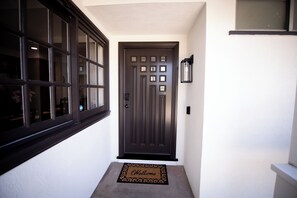 A dark brown front door with a decorative panel, a doormat with 'Welcome' text, and a wall-mounted light fixture. - Family friendly 3-bedroom house with AC in Huntington Beach (Huntington Beach)