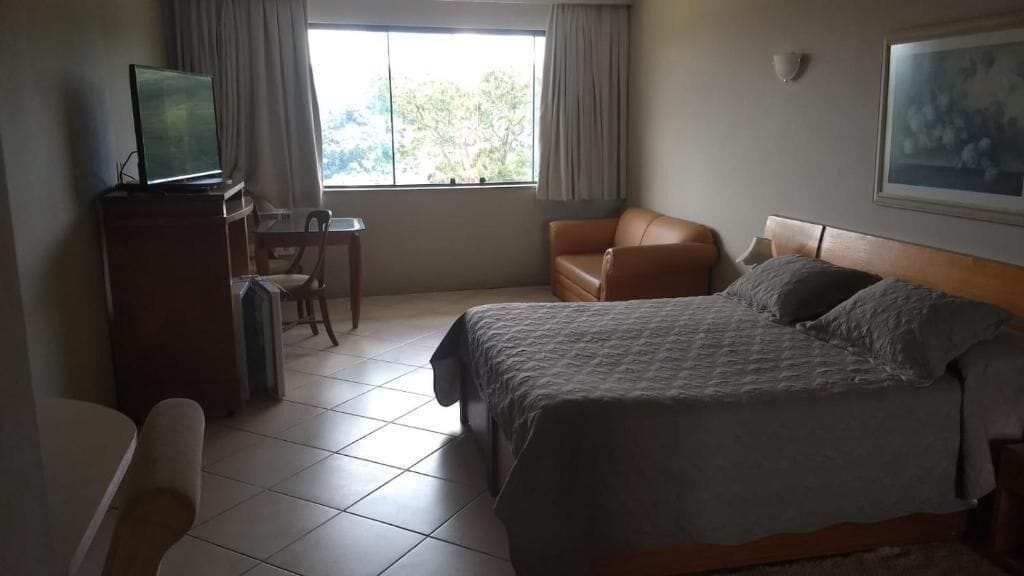 A hotel room with a bed, a desk, a chair, and a television.