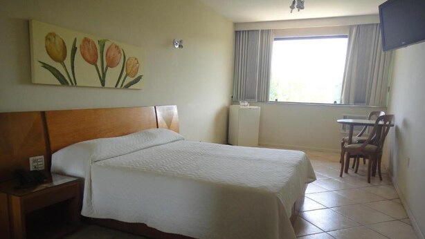 Una habitación de hotel con cama, escritorio, silla, radiador y ventana con cortinas.