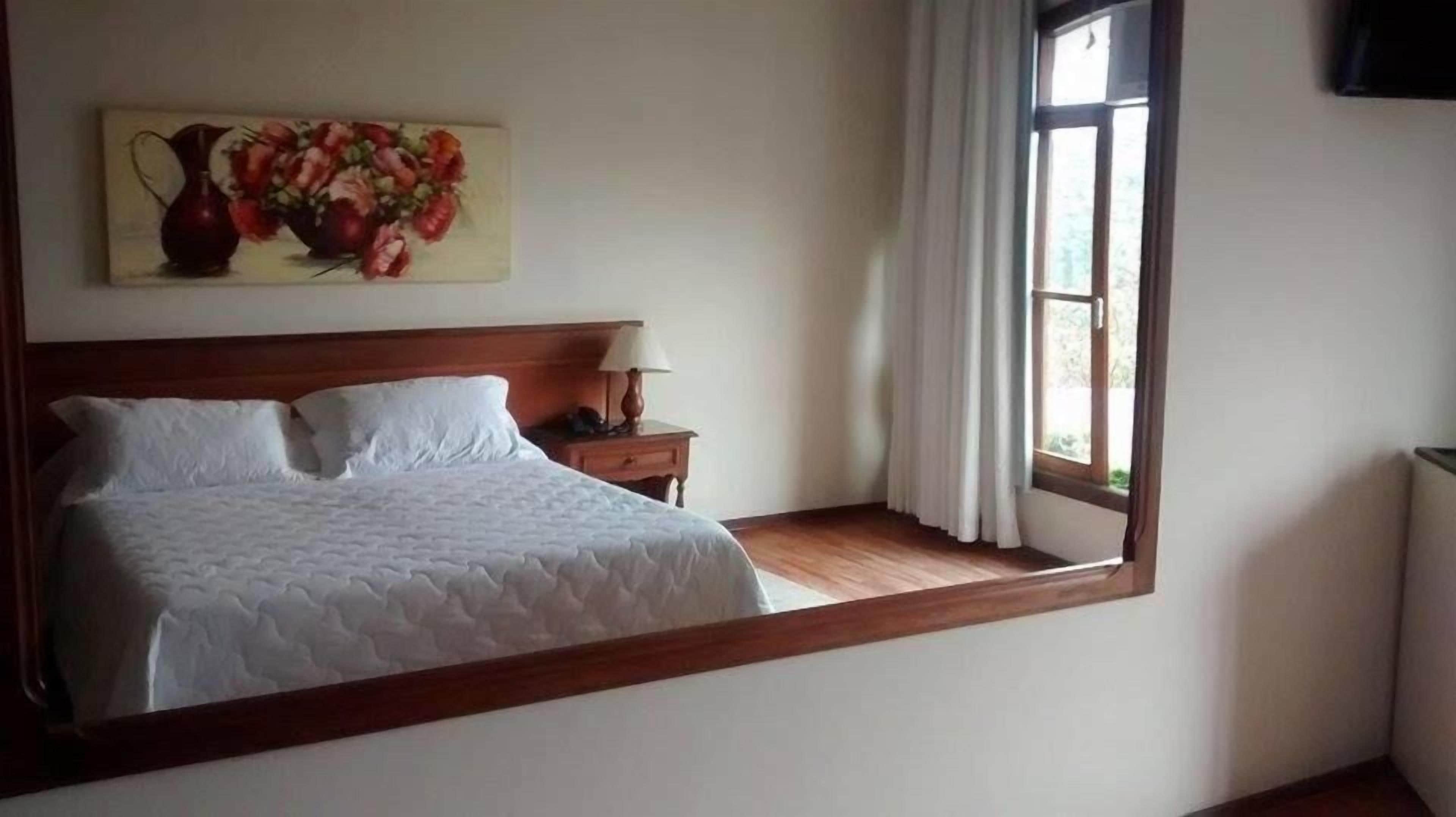 Un dormitorio con una cama, una mesita de noche, una lámpara, un cuadro y una ventana.